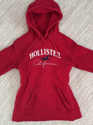 Hollister hoodie  - Röd hoodie från Hollister California med tryck på framsidan. Skriv om ni har frågor osv🩷