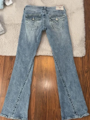 True religion jeans strl 26 - Säljer ett par true religion  jeans med snygga detaljerade bakfickor och kontrastsömmar. Jeansen har en klassisk femficksmodell och är tillverkade i slitstark denim. Perfekta för dig som gillar en avslappnad men trendig stil.
