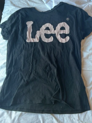 Svart Lee t-shirt med stor logga - Säljer en svart t-shirt från Lee med stor vit logga framtill. Klassisk rund halsringning och korta ärmar. Tillverkad i mjuk bomull för skön känsla. Perfekt till jeans eller shorts för en avslappnad look.