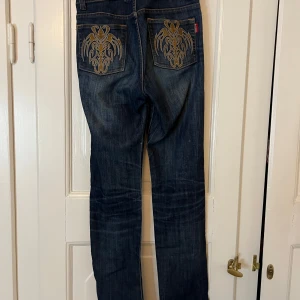 Jeans med snygga fickor  - Snygga, raka, mörkblå jeans med unika broderade mönster på bakfickorna. De har en klassisk femficksdesign och en bekväm passform. Perfekta för en stilren look. Jag är 173cm