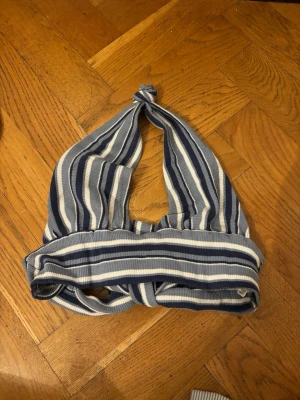 Blåvit randig halterneck topp - Säljer en ribbad halterneck topp med blå och vita ränder. Toppen har bred resår under bysten och knyts i nacken för en snygg passform. Perfekt för dig som gillar en sportig och trendig stil.