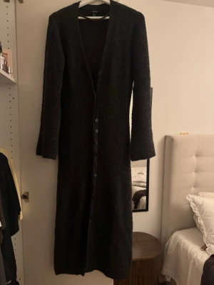 Lång mörkgrå stickad kofta/klänning Vero Moda - Lång stickad kofta i mörkgrått med knappar hela vägen framtill. Koftan har v-ringning och långa ärmar. Helt ny aldrig använd. Storlek M men passar också S. Nypris: 749kr. 