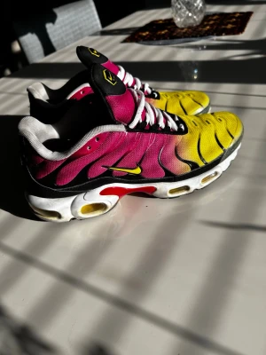 Nike Air Max Plus TN rosa/gul - Nike Air Max Plus TN sneakers i en grym färgkombination av rosa, gul och svart med vita detaljer. Skorna har en mesh-överdel, vita snören och den ikoniska TN-loggan på plösen. Sulan är vit med gula och röda inslag och synlig Air. Storlek 42, fraktas dagen de köps.
