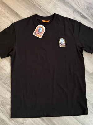 Svart t-shirt  - Svart t-shirt  med rund hals och korta ärmar. På bröstet sitter ett broderat märke med texten 'PJS Anchorage' och en logga i gult, rött och blått. Tillverkad i mjuk bomull för en bekväm känsla. Passar M eventuellt S. Tar emot rimliga bud! Aldrig använd.