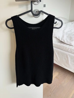 Svart ribbad stickad linnetopp - Säljer en svart ribbad stickad linnetopp med breda axelband och rund halsringning. Toppen har en snygg struktur i stickningen och är perfekt för att styla lager på lager eller bära som den är. Enkel men trendig design som passar till mycket.