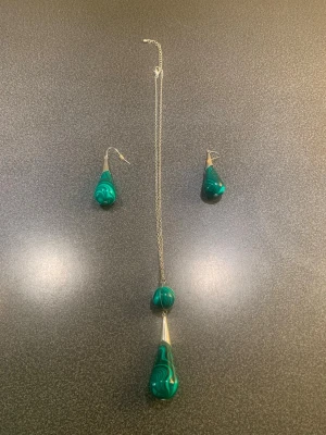 Set med halsband och örhängen i grön sten - Snyggt smyckeset med halsband och matchande örhängen. Både halsbandet och örhängena har droppformade hängen i grön mönstrad sten och detaljer i silverfärgad metall. Kedjan är tunn och stilren. Perfekt för dig som gillar unika accessoarer med färg.