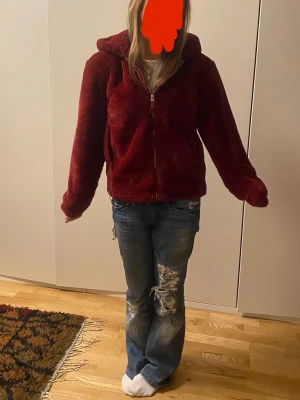 Vinröd teddyjacka med huva - Mysig vinröd teddyjacka med dragkedja och huva. Jackan har en fluffig, mjuk yta och avslappnad passform. Jackan är köpt secondhand för 1100 i perfekt skick från märket Kiabi i sorlek S men passar mer M! Mycket varmare än man tror men passar perfekt nu till våren men också höst och tidig vinter! Skriv för mer bilder eller frågor