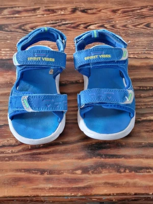 Blå, blinkande sandaler - Använda en sommar. Det är lite trådar som hänger vid remmarna och den översta remmen är inte fastsydd längst ut med kardborren. Ser ut som en produktionsfel för syns Inga hål efter en söm. Går säkert att limma fast om det skulle störa. Stl 28