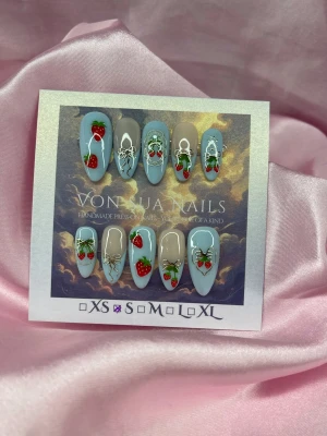 BerryCharm (S);Medium Almond - Handgjorda press-on naglar i en medium mandelform. Naglarna har en ljusblå och nude bas med detaljerade  jordgubbar, guldiga rosetter och blad. Perfekt för dig som vill ha en söt och unik nageldesign. S: 15 mm, 11,5 mm, 12 mm, 11 mm, 9 mm 