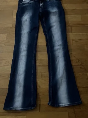 Mörkblå bootcut jeans med slitningar - Säljer ett par mörkblå bootcut jeans med snygga slitningar och tvättade detaljer framtill och baktill. Jeansen har klassiska fem fickor och breda ben. Perfekta för dig som gillar retrostil och vill ha ett par jeans som sticker ut. Cheap monday lappen har åkt av och därav kan vi diskutera pris