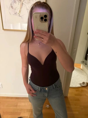 Vinröd body HM - Säljer en vinröd body med djup v-ringning och smala axelband. Sitter tight och har en enkel, stilren design utan synliga detaljer eller mönster. Perfekt att styla med jeans eller kjol för en trendig look.