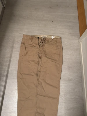 Beige chinos med rak passform - Snygga beige chinos med rak passform och klassisk design. Byxorna har framfickor och bälteshällor i midjan. Perfekta för en clean och avslappnad stil. Tillverkade i ett mjukt bomullsmaterial som känns skönt mot huden.