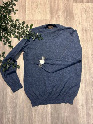 Blå stickad tröja från Oscar Jacobson - Mörkblå stickad tröja från Oscar Jacobson i mjukt material. Tröjan har rund halsringning, långa ärmar och ribbade muddar vid ärmslut och nederkant. Enkel och stilren design som passar perfekt till jeans eller chinos.