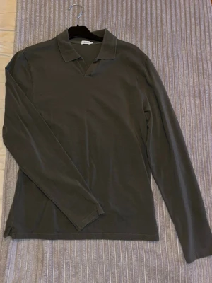 Mörkgrön piké från Filippa K - Stilren mörkgrön långärmad piké från Filippa K med klassisk krage och v-ringning. Tillverkad i mjukt material som känns skönt mot huden. Perfekt för en clean och avslappnad look.