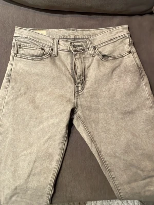 Grå Levi's jeans med vintagekänsla - Säljer ett par gråa Levi's jeans med klassisk femficksmodell och raka ben. Jeansen har en snygg tvättad look och detaljer som den ikoniska röda Levi's-lappen och läderpatch bak i midjan. Perfekta för dig som gillar en avslappnad och tidlös stil. Väldigt bra skick och sällan använda. 