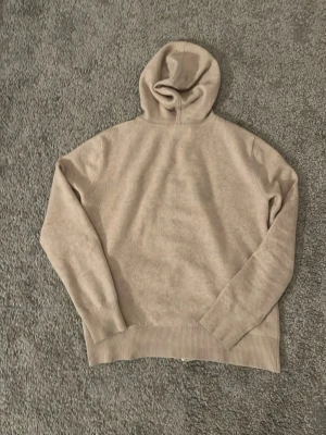 CASHMERE ZIP XXS - Säljer en stilren beige hoodie från sayless med dragkedja framtill och ribbade muddar. Hoodien har en mjuk känsla . Perfekt för dig som gillar en clean och enkel look.