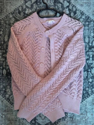 Ljusrosa kofta från Gina Tricot - Supersöt ljusrosa kofta från Gina Tricot med genombrutet stickat mönster och stora matchande knappar framtill. Koftan har ribbade muddar vid ärmslut och nederkant samt rund halsringning. Perfekt för lager på lager och en feminin touch till din outfit. Passar storlek XS och S