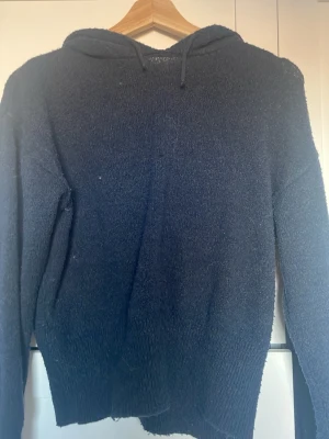 Mörkblå fluffig hoodie - Mysig mörkblå hoodie med huva och långa ärmar. Tillverkad i ett stickat material, perfekt för dig som gillar en avslappnad och chill stil. Ribbstickade muddar vid ärmslut och nederkant ger en snygg passform.