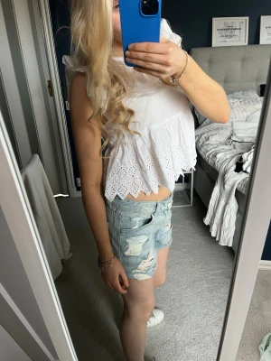 Ljusblå slitna jeansshorts - Säljer ett par ljusblå jeansshorts med slitna detaljer och råa kanter. Shortsen har klassisk femficksdesign och är midwaist. Perfekta för varma dagar och ger en avslappnad look.