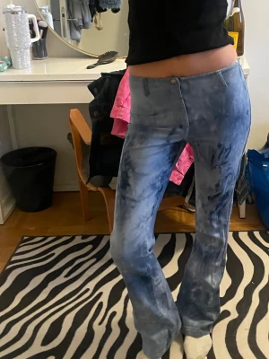 Blå tie-dye utsvängda jeans - Säljer ett par blå tie-dye byxor  med utsvängda ben och medelhög midja. Jeansen har en cool tvättad look och sitter tajt upptill. Perfekta för dig som vill sticka ut lite extra med din outfit!