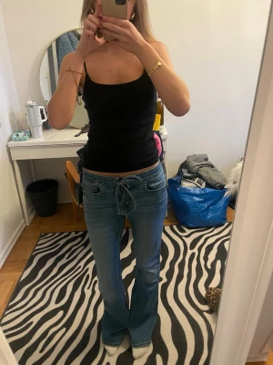 Blå bootcut jeans med snörning - Säljer ett par blå bootcut jeans med snörning i midjan. Jeansen har klassiska fickor bak och fram, och är tillverkade i ett mjukt denimtyg. Perfekta för dig som gillar en avslappnad men trendig look.