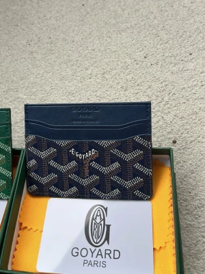 Mörkblå kortfodral från Goy4ard - Snyggt mörkblått kortfodral från Goy4ard med det klassiska mönstret i vitt och beige. Fodralet har flera kortfack och är tillverkat i exklusivt läder med canvasdetaljer. Perfekt för dig som vill ha en stilren och lyxig accessoar.