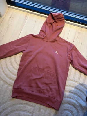 Rosa hoodie från Adidas - Säljer en snygg rosa hoodie från Adidas som har märket över bröstet. Funkar super bra till träning då den inte är super tjock i materialet. Aldrig använd.