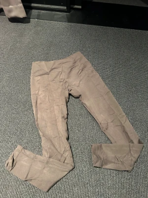 Bruna leggings från Relode - Säljer ett par bruna leggings från Relode med hög midja och stretchigt material. De har en enkel, stilren design utan fickor och loggan syns tydligt i midjan. Perfekta för träning eller chill. Materialet känns mjukt och följsamt.