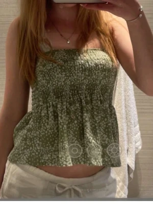Grön blommig bandeau topp - Söt bandeau topp i ljusgrönt med små vita blommor. Smockad upptill för skön passform och volang nedtill. Den är från Gina tricot i st XS🤍🤍