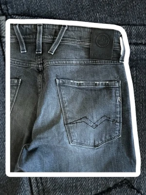 Replay anbass - Snygga gråa jeans från Replay med raka ben och klassiska bakfickor med broderad detalj. Jeansen har bälteshällor och en svart Replay-lapp i midjan. Perfekta för dig som gillar en stilren och tidlös look.