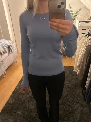 Ljusblå tröja med knappar - Ljusblå tröja med rund hals och långa ärmar. Tröjan har ribbade muddar och tre dekorativa silverknappar vid ärmsluten. Snygg och enkel modell som passar till mycket. Aldrig använd