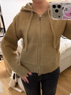 Beige hoodie med dragkedja från ZARA - Mysig beige hoodie med dragkedja framtill och två stora fickor. Tröjan har ribbade muddar, huva med dragsko och är tillverkad i ett mjukt stickat material. Perfekt för en avslappnad och stilren look.
