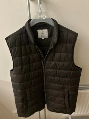 Svart dunväst från Bläck - Snygg brun dunväst från Bläck med quiltad design och hög krage. Västen har dubbel dragkedja framtill och två fickor på sidorna.