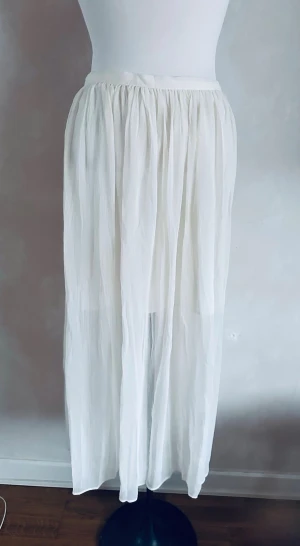 Vit långkjol från H&M i polyester - Luftig och flowy vit långkjol från H&M i 100% polyester. Kjolen har ett tunt, lätt material med mjuka veck och resår i midjan för skön passform. Perfekt för varma dagar och enkel att styla med olika toppar.