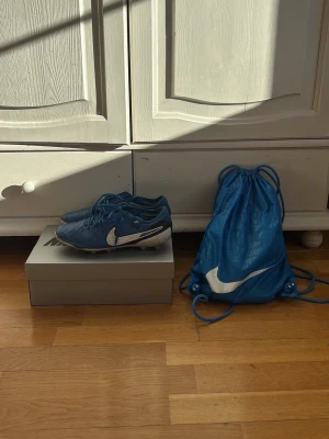 Nike tiempo elite - Säljer ett par blå Nike fotbollsskor med vita detaljer och snörning. Skorna har en klassisk låg profil och är tillverkade i syntetmaterial för bra bollkontroll. Medföljer gör en matchande blå Nike gympåse. Perfekta för dig som vill sticka ut på planen! Nypris runt 3000