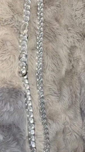 Flätat silverfärgat bälte - Snyggt flätat bälte i metallic silverfärg med rundad metallspänne. Bältet har en smal design och är gjort i ett glansigt material som ger en cool och trendig look. Perfekt för att lyfta vilken outfit som helst.