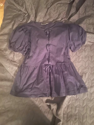 Mörkblå blus med puffärmar från Gina  - Snygg mörkblå blus med puffiga kortärmar och knytband framtill. Blusen har en lös passform och volang nedtill som ger en trendig siluett. Perfekt att styla med jeans eller kjol för en cool look. använd några gånger och är i storlek 158/164💓💓