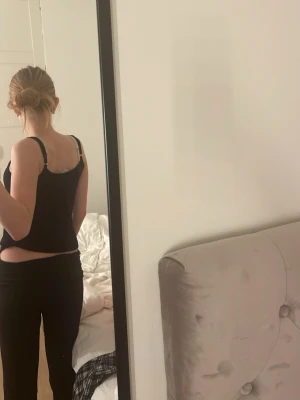 Svart spetsdetaljerad linnetopp - Säljer en svart linnetopp med tunna axelband och fina spetsdetaljer längs urringningen. Toppen har en enkel och stilren design som passar perfekt till jeans eller kjol. Superenkel att styla och ett måste i garderoben! Den funkar även som ett natt linne, linnet har ett mjukt och lent material 