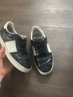 Valentino flycrews - Snygga sneakers från Valentino Garavani i mörkblått och vitt skinn. Klassisk låg modell med svarta skosnören och rund tå. Perfekta för dig som vill ha en stilren och exklusiv look. Storlek 39 men passar upp till 41 skulle jag säga. Priset kan förhandlas vid snabb affär!
