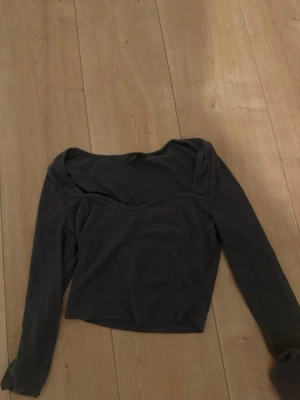 Svart croppad långärmad topp - Grå svart croppad topp med lång ärm och v-ringad halsringning. Tillverkad i ett mjukt, stretchigt material som sitter snyggt på kroppen. Perfekt att matcha med höga jeans eller kjol.