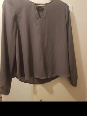 Grå långärmad blus med v-ringning - Stilren grå blus med lång ärm och avslappnad passform. Blusen har en djup v-ringning och är tillverkad i ett mjukt, lätt tyg som ger ett snyggt fall. Perfekt att matcha med jeans eller kjol för en enkel men trendig look. Storlek: s/m