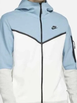 Nike blåvit hoodie med dragkedja - Nike hoodie i ljusblått och vitt med svart dragkedja och logga på bröstet. Hoodien har huva, svarta detaljer och en praktisk ficka med dragkedja på ärmen. Tillverkad i mjukt material som passar perfekt för en avslappnad stil.