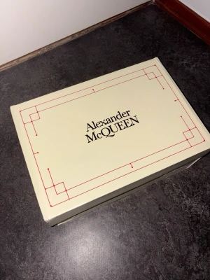 Alexander McQueen svarta sneakers - Säljer ett par svarta Alexander McQueen sneakers med vit tjock sula och vit detalj på hälen. Skorna har klassisk låg siluett, svarta skosnören och guldfärgad logga på plösen. Tillverkade i slätt läder för en clean och lyxig look.     Pris kan diskuteras!