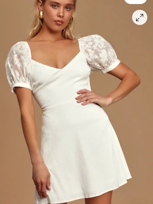 Vit kortklänning med puffärmar - Helt oanvänd med prislappar kvar och allt. Supersöt vit kortklänning med v-ringning och puffiga, transparenta kortärmar med blommigt mönster. Klänningen har en figurnära passform upptill och lätt utställd kjol. Perfekt för sommarens alla tillfällen!