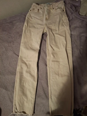 Beiga raka jeans från 157 - Snygga beiga jeans från 157 med rak passform och råa kanter vid bensluten. Klassisk femficksmodell och bälteshällor. Tillverkade i ett mjukt bomullsmaterial som är skönt att bära. Perfekta för en avslappnad och trendig look. Har även en röd nagellacks fläck som du kan se på sista bilden