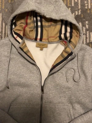 Grå burberry hoodie - Säljer en stilren hoodie från burberry som är bästa kvaliten. Den har sjuka detaljer som burberry färgen på insidan. Perfekt året runt och materialet är tjock o hållbar. Oanvänd.