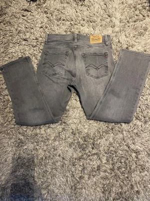 Grå jeans från Replay - Snygga grå jeans från Replay med raka ben och klassiska bakfickor med broderad detalj. Jeansen har en läderpatch med Replay-logga bak i midjan och är tillverkade i mjukt denimtyg. Perfekta för en avslappnad och trendig look.