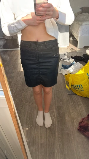 Svart kortkjol i denim - Säljer en svart kortkjol i denim med klassisk femficksdesign och normal passform. Kjolen har bälteshällor och stängs med dragkedja och knapp framtill. Perfekt basplagg till garderoben!