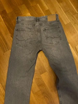 Grå raka jeans från Jack & jones - Snygga grå jeans från Jack & Jones med raka ben och klassisk femficksmodell. Jeansen har hög midja och är tillverkade i ett slitstarkt bomullsmaterial. Perfekta för en avslappnad och trendig stil.