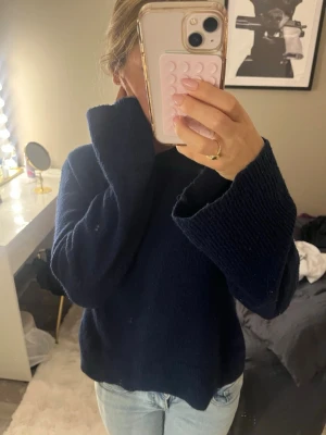 Mörkblå stickad tröja med vida ärmar - Mysig mörkblå stickad tröja med rund halsringning och extra vida ärmar. Tröjan har en avslappnad passform och är perfekt att bära till jeans. Materialet känns mjukt och värmande, perfekt för kyligare dagar.